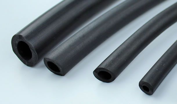 Un primer plano de cuatro tubos de goma negros sobre una superficie blanca.