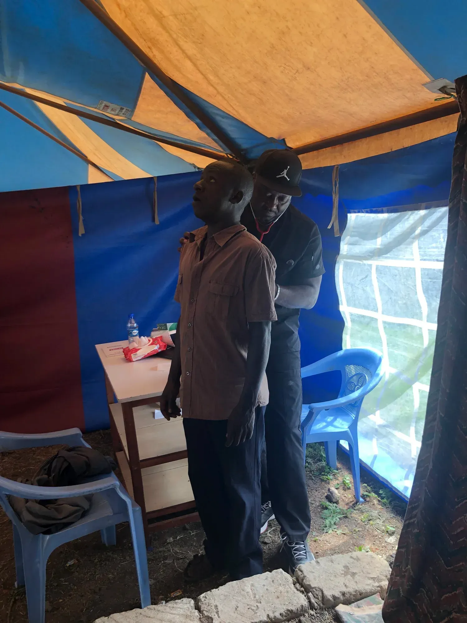 A health worker examines a patient inside a tent with blue and yellow walls.