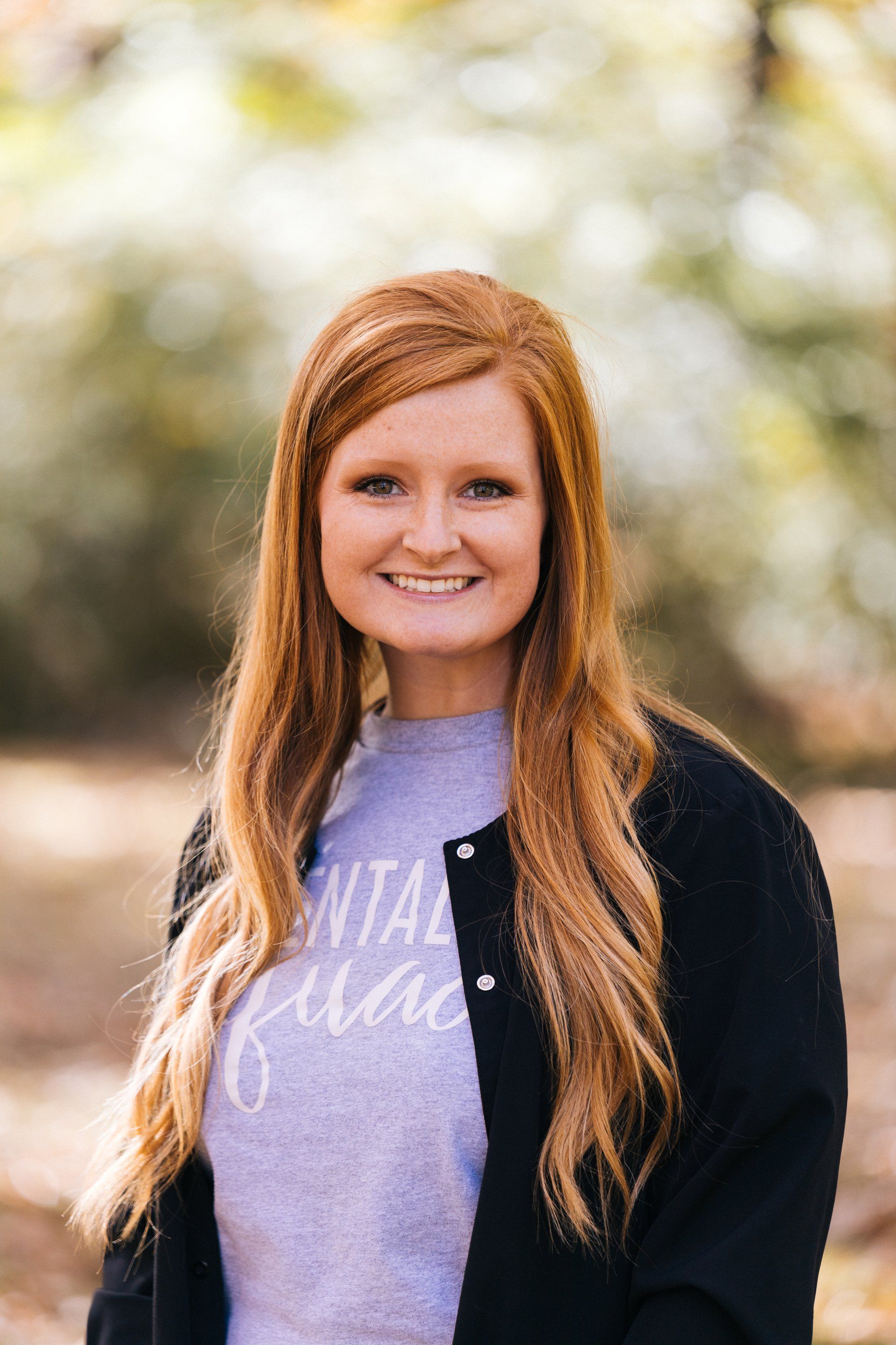 A woman with long red hair is wearing a purple shirt and a black jacket.