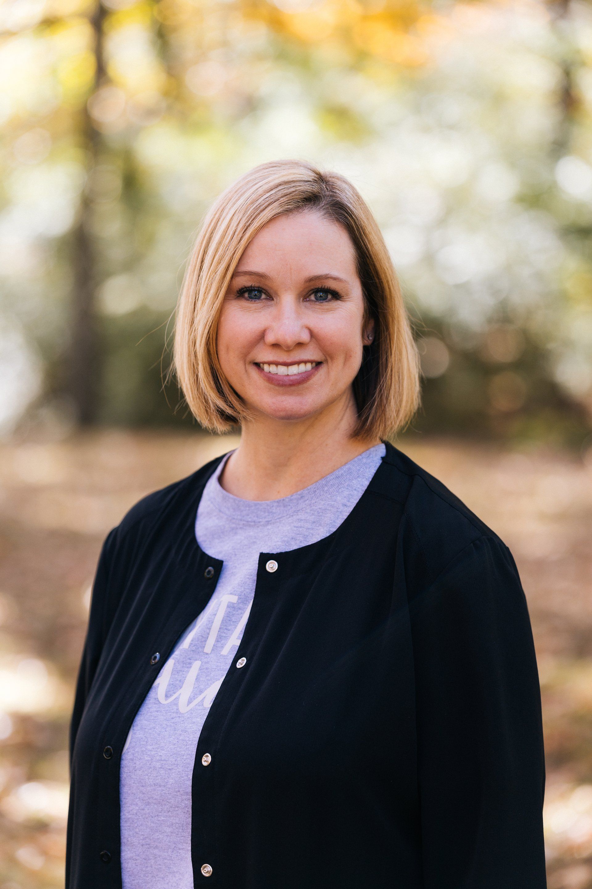 A woman wearing a black cardigan and a purple sweater is smiling for the camera.