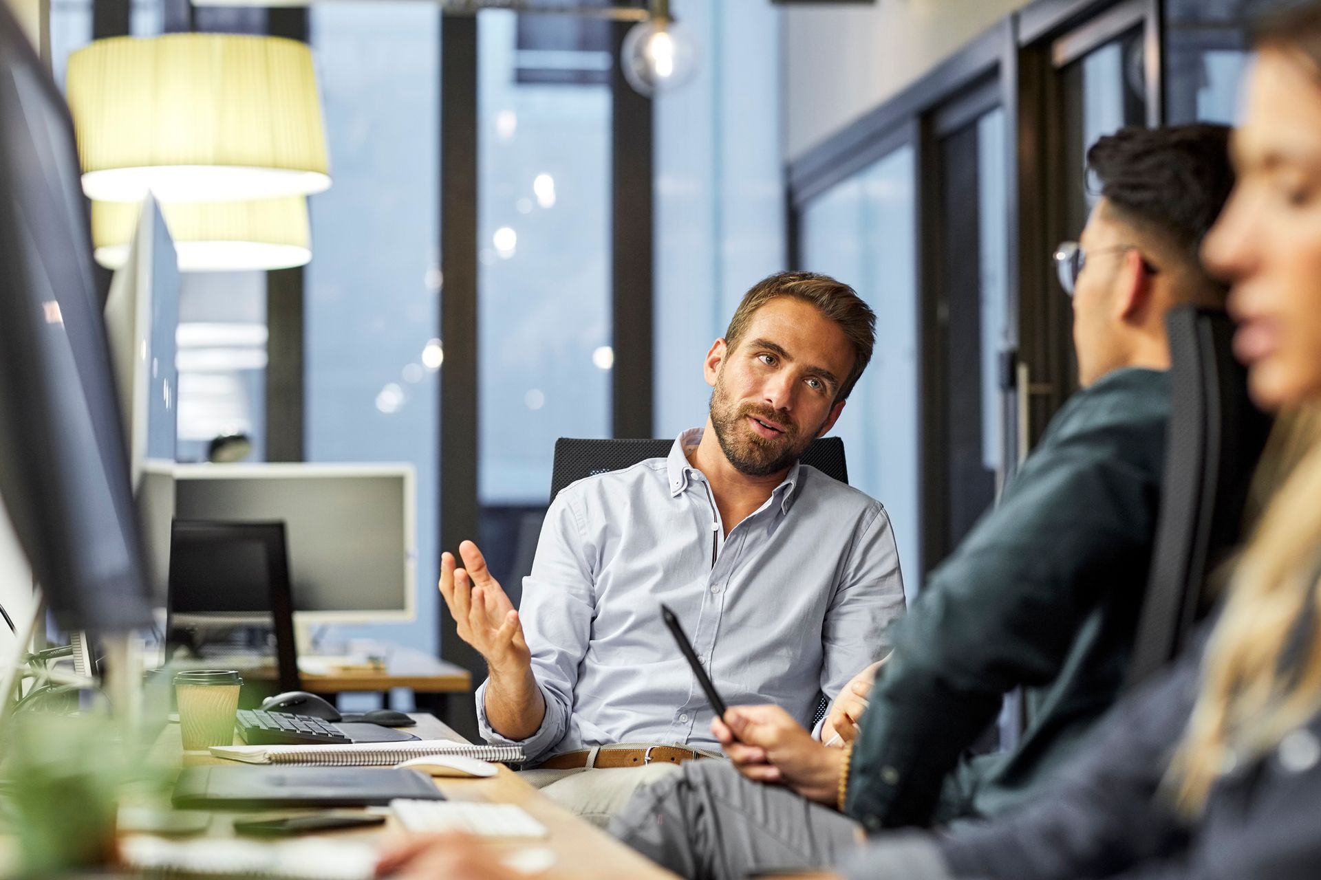 A man is sitting at a desk talking to a group of people in an office. A man is sitting at a desk talking to a group of people in an office.