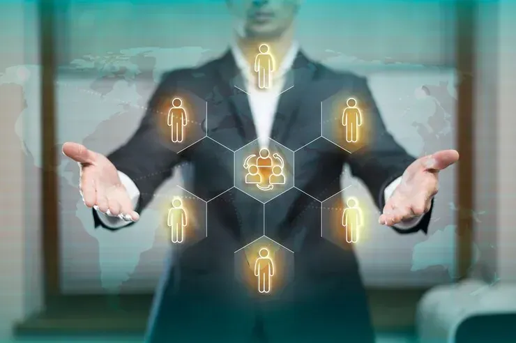 A man in a suit is holding his hands out in front of a screen with people icons on it.