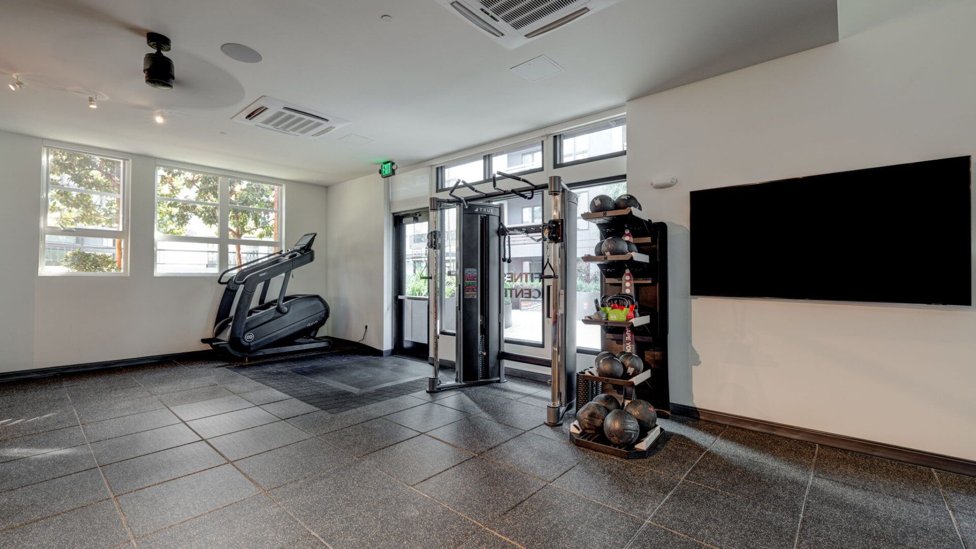 Gym with fitness equipment, natural light, and a large screen TV at The Waymark in Walnut Creek, CA.