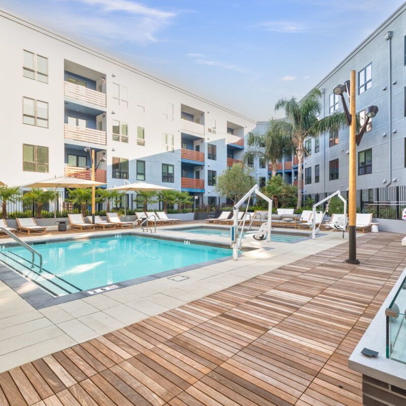 Swimming pool and lounge area with wood deck, next to white apartment buildings. Sunny day at The Waymark in Walnut Creek, CA.
