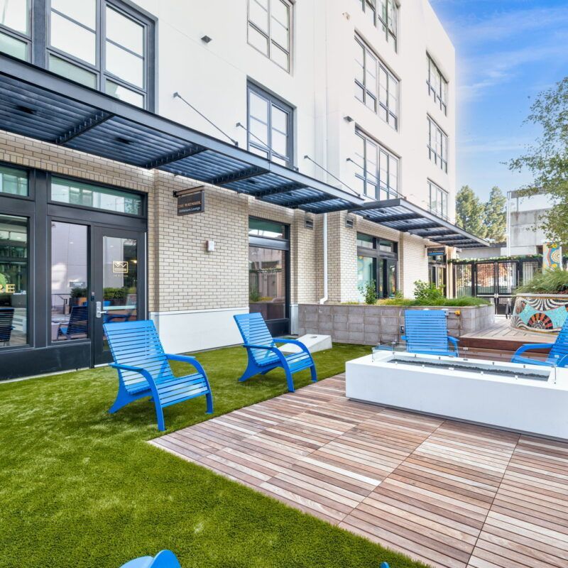 Outdoor patio with blue chairs, a fire pit, and a building with a brick facade at The Waymark in Walnut Creek, CA.