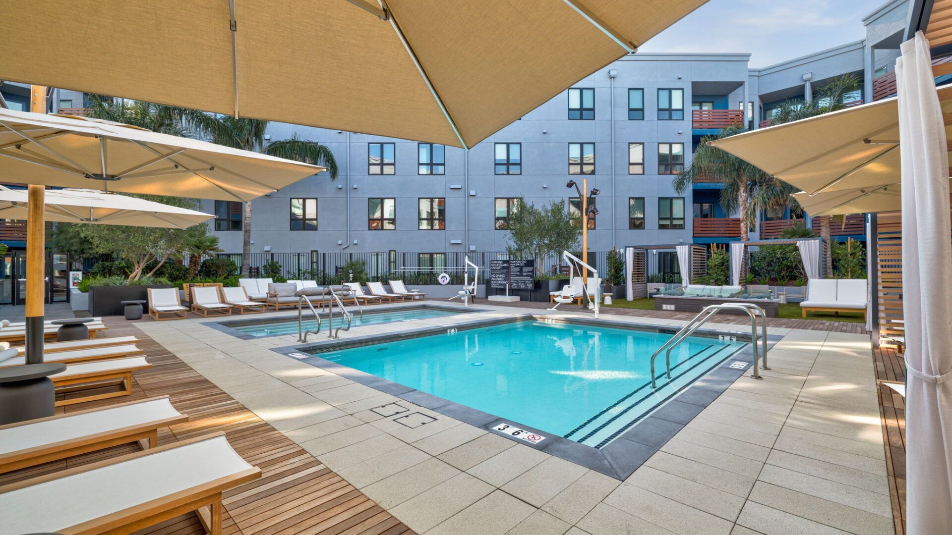 Pool area with lounge chairs, umbrellas, and a multi-story apartment building at The Waymark in Walnut Creek, CA.