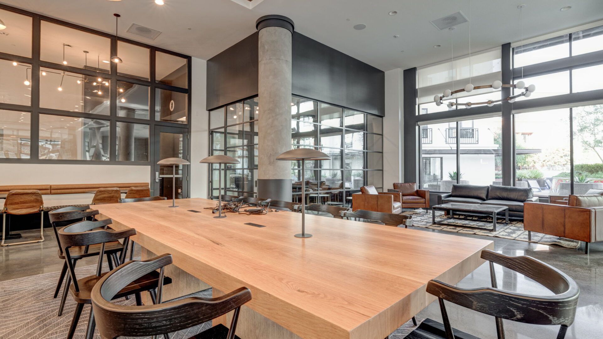 Modern lounge with a long wooden table and chairs, large windows, and a seating area at The Waymark in Walnut Creek, CA.
