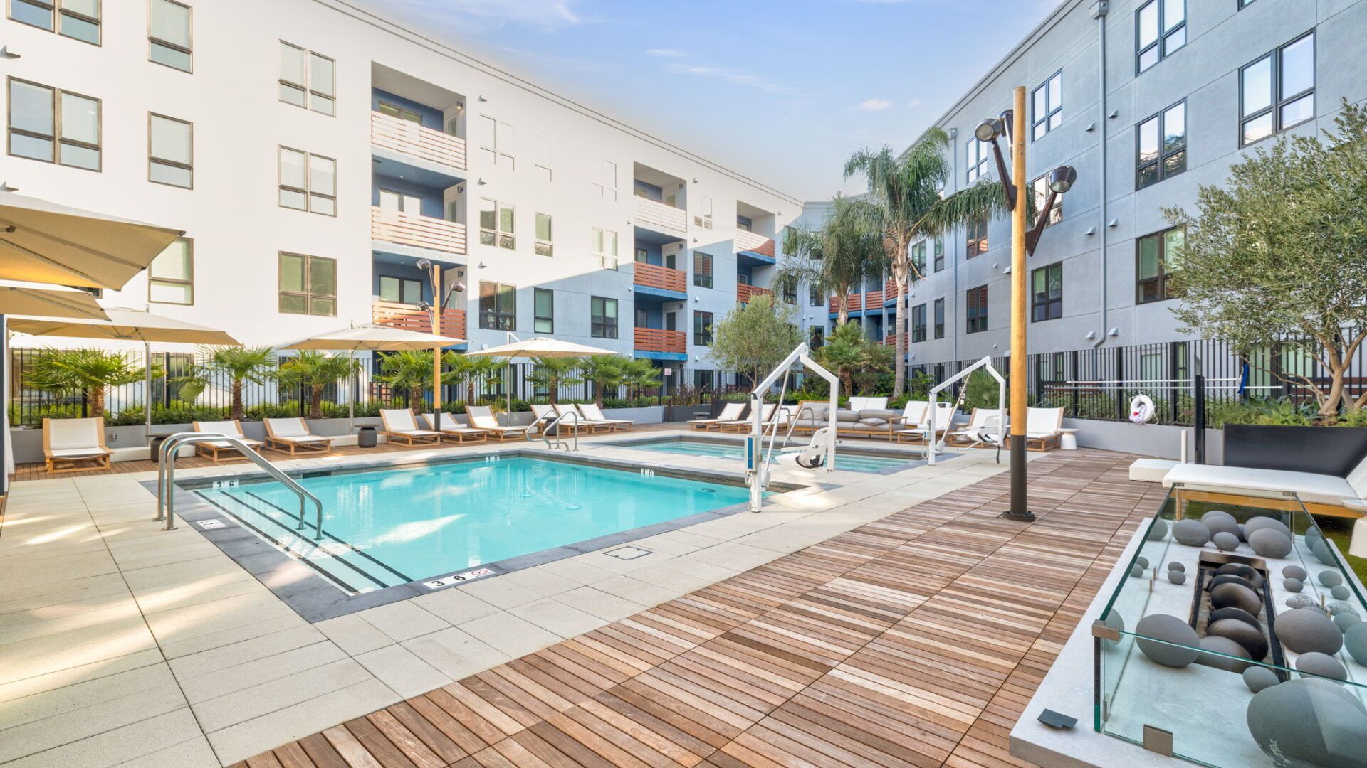 Pool area at an apartment complex with lounge chairs, umbrellas, and a fire pit at The Waymark in Walnut Creek, CA.