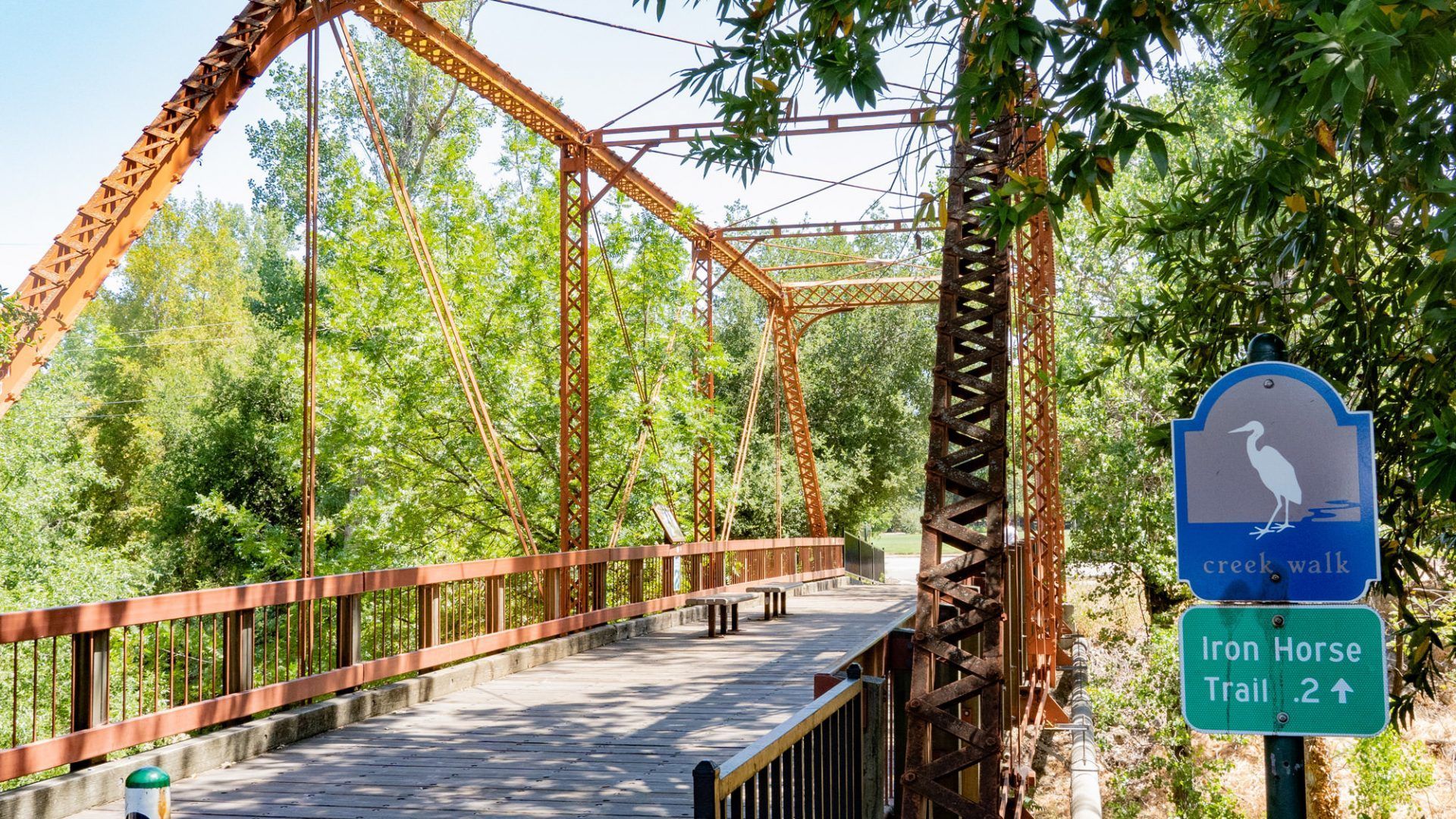 Rusty metal bridge over a river, Iron Horse Trail marker in view at The Waymark in Walnut Creek, CA.
