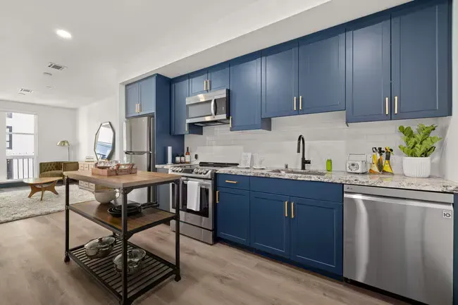 Modern kitchen with navy blue cabinets, stainless steel appliances, and island, hardwood floors.