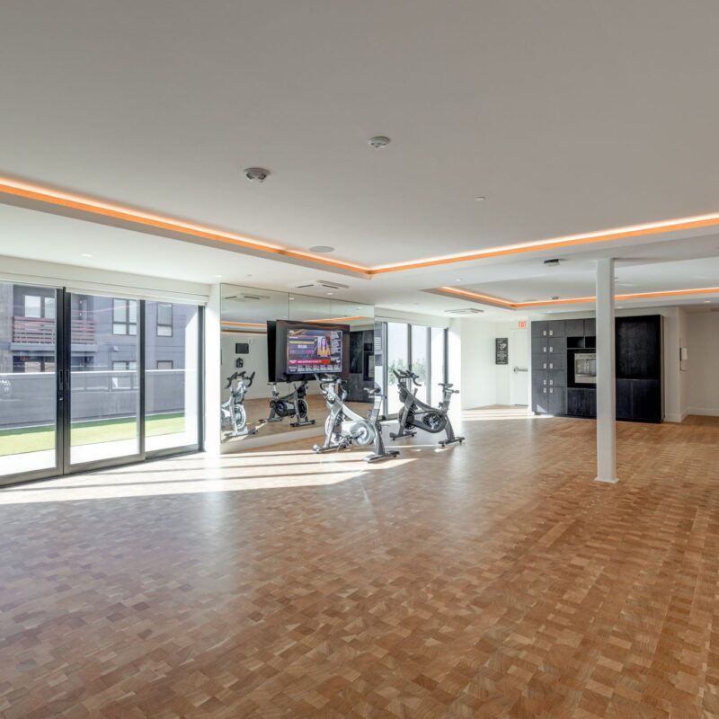 Gym with spin bikes, mirrors, TV, and wooden floor, with exterior view through windows at The Waymark in Walnut Creek, CA.