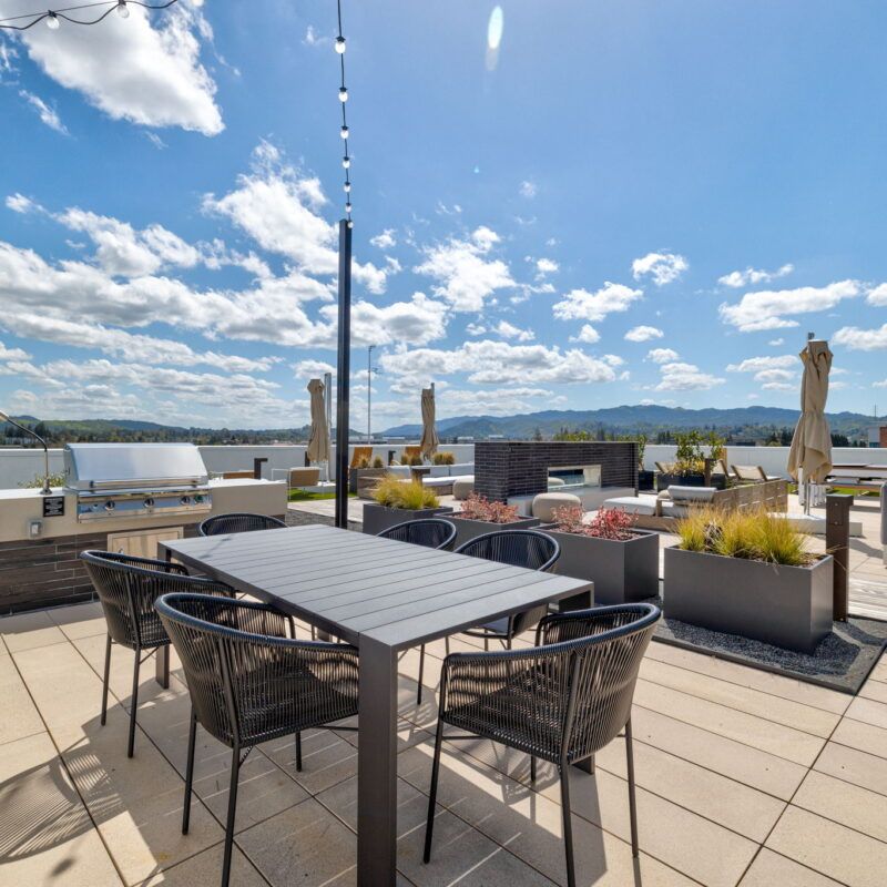Rooftop patio with table, chairs, grill, and fire pit, under blue sky with clouds at The Waymark in Walnut Creek, CA.