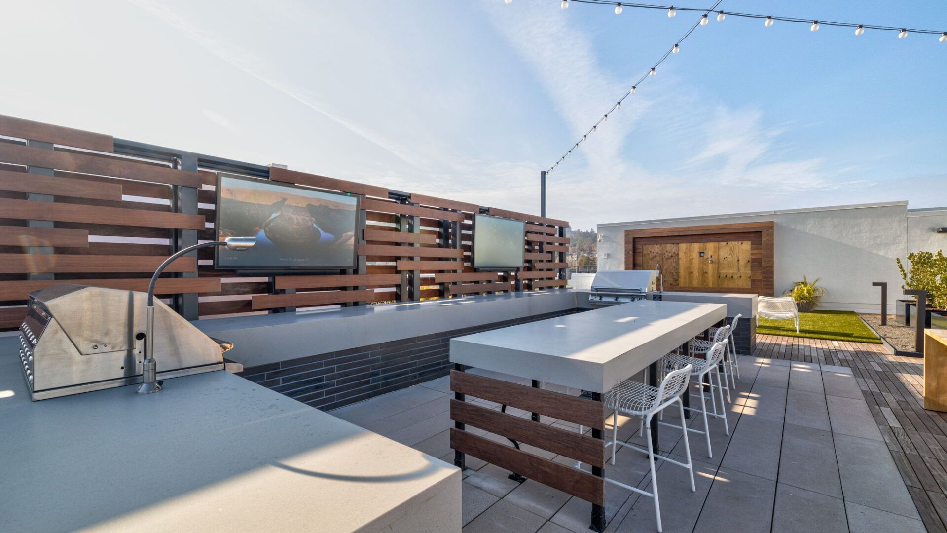 Rooftop patio with outdoor kitchen, TVs, and bar seating under a blue sky at The Waymark in Walnut Creek, CA.