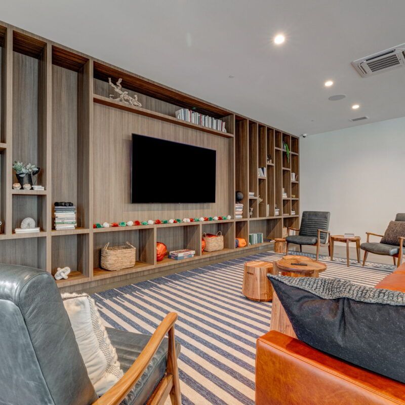 Living room with built-in bookshelves, TV, leather furniture, striped rug, and decorative items at The Waymark in Walnut Creek, CA.