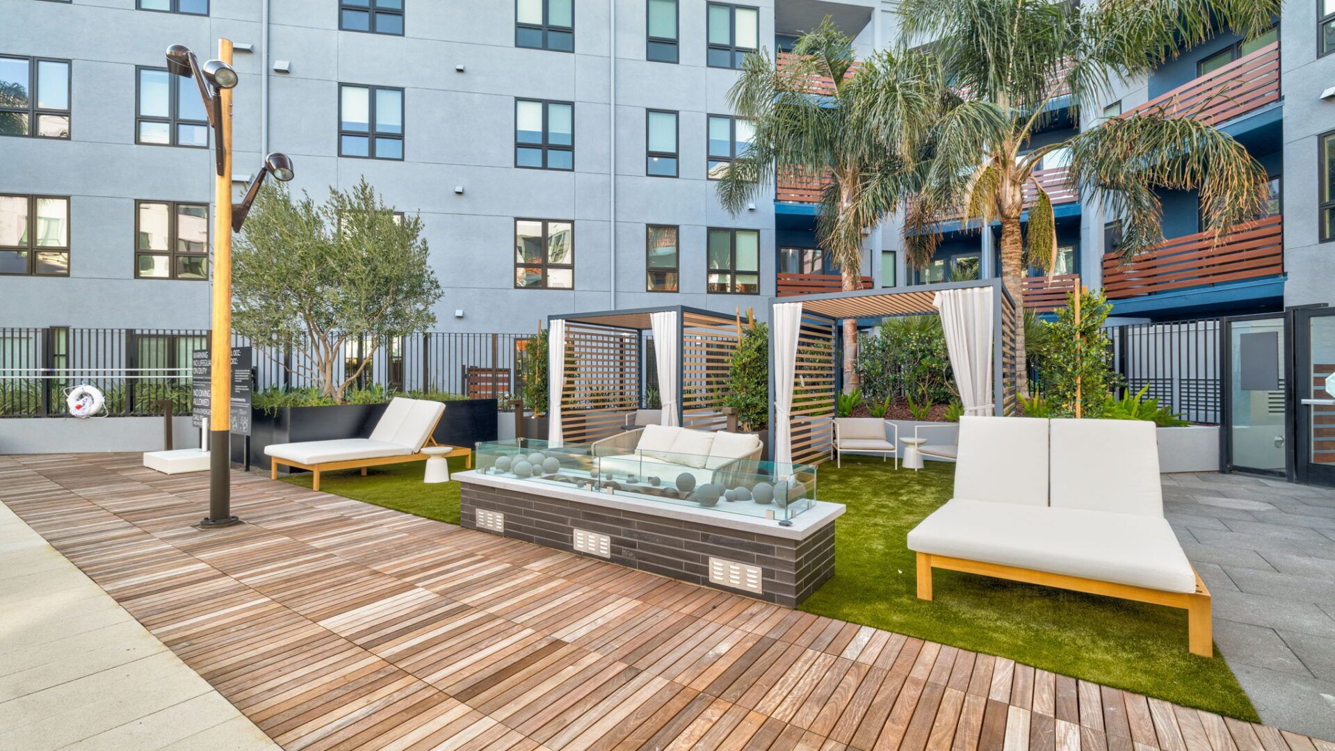 Outdoor lounge area with wooden deck, lounge chairs, fire pit, and apartment building in background at The Waymark in Walnut Creek, CA.