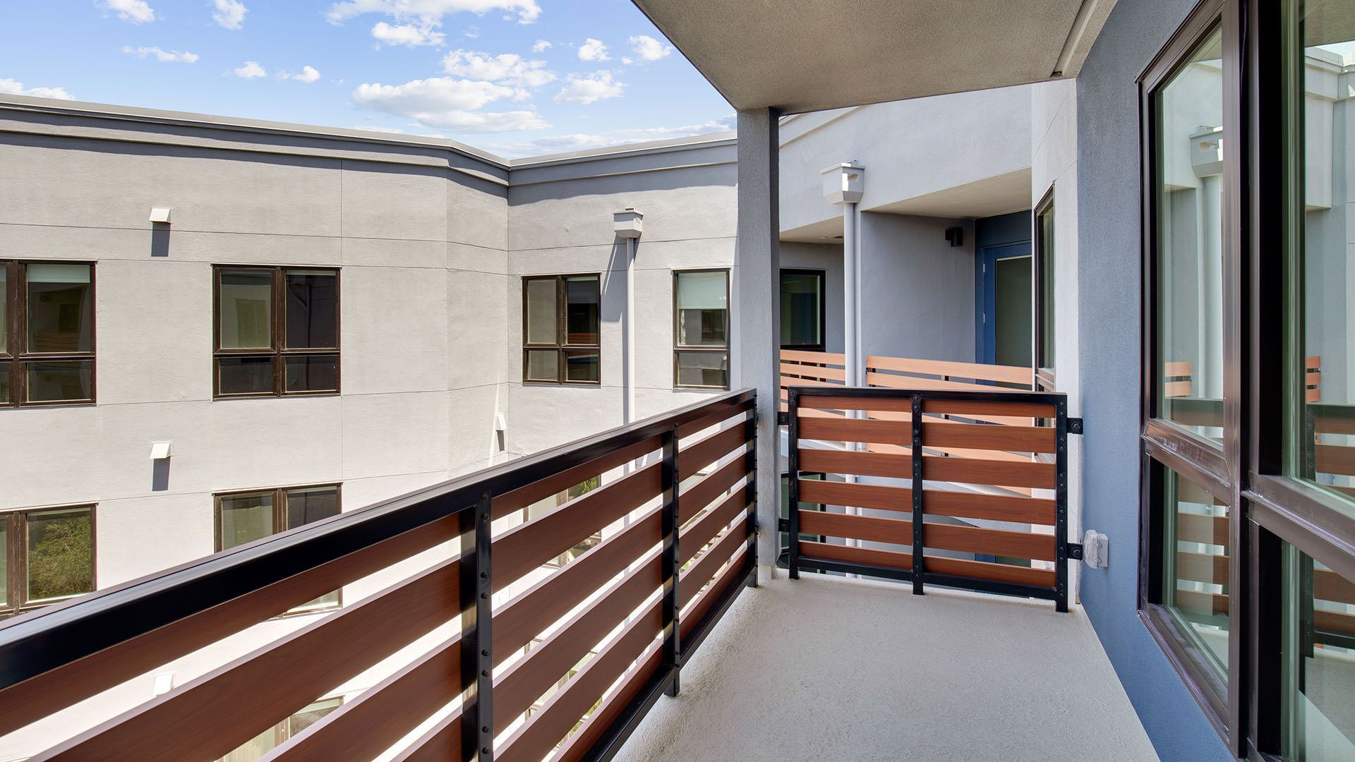 Balcony with brown horizontal railing, facing an apartment building with many windows at The Waymark in Walnut Creek, CA.