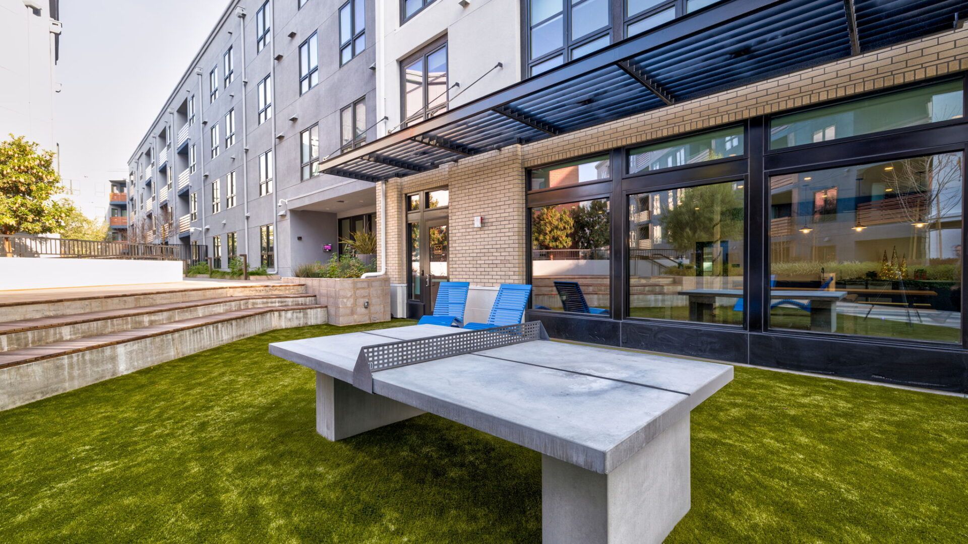 Outdoor area with ping pong table on artificial grass, with apartment building in the background at The Waymark in Walnut Creek, CA.