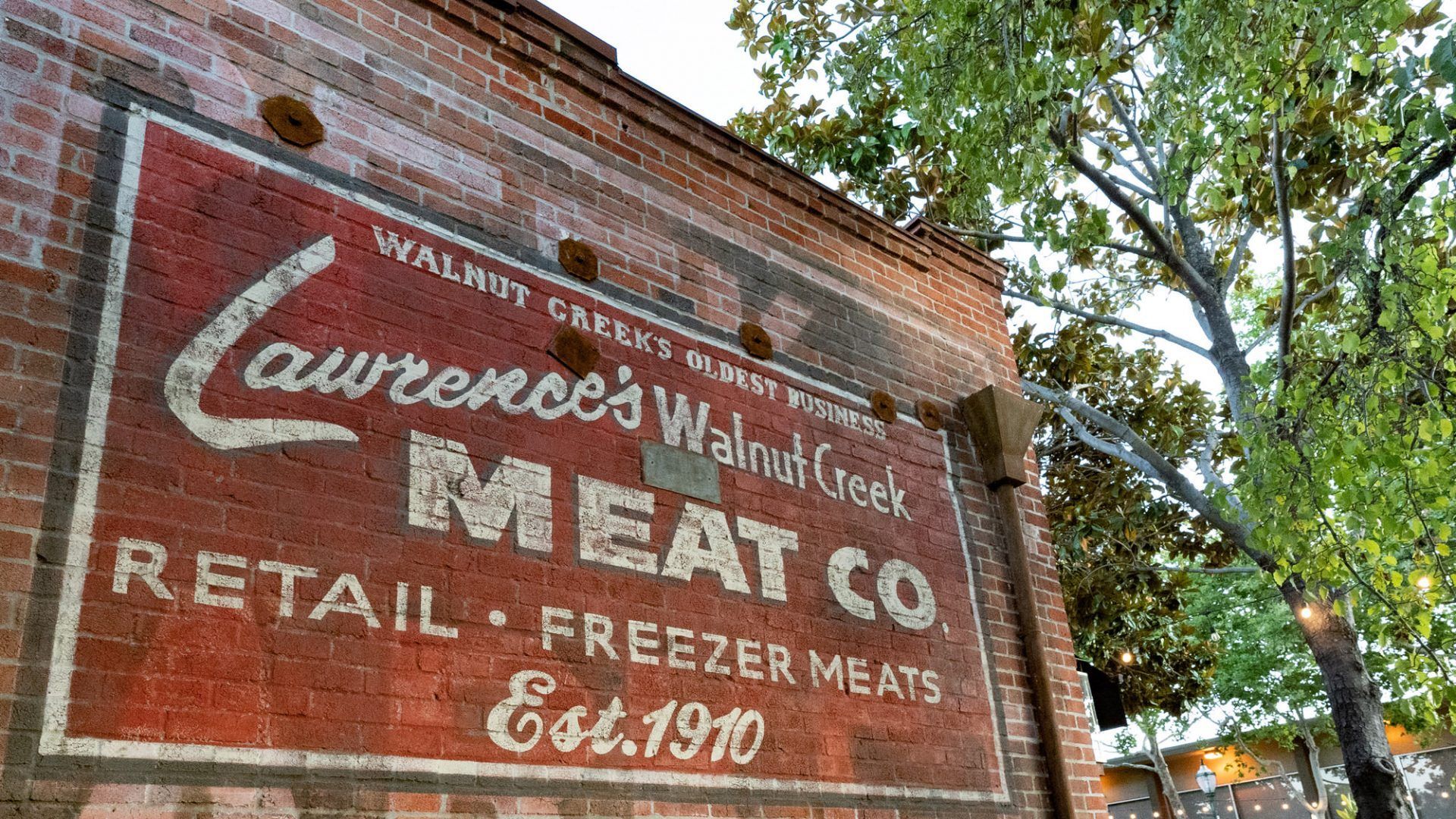 Sign for Lawrence's Walnut Creek Meat Co. painted on brick wall. Red and white text. Est. 1910 at The Waymark in Walnut Creek, CA.