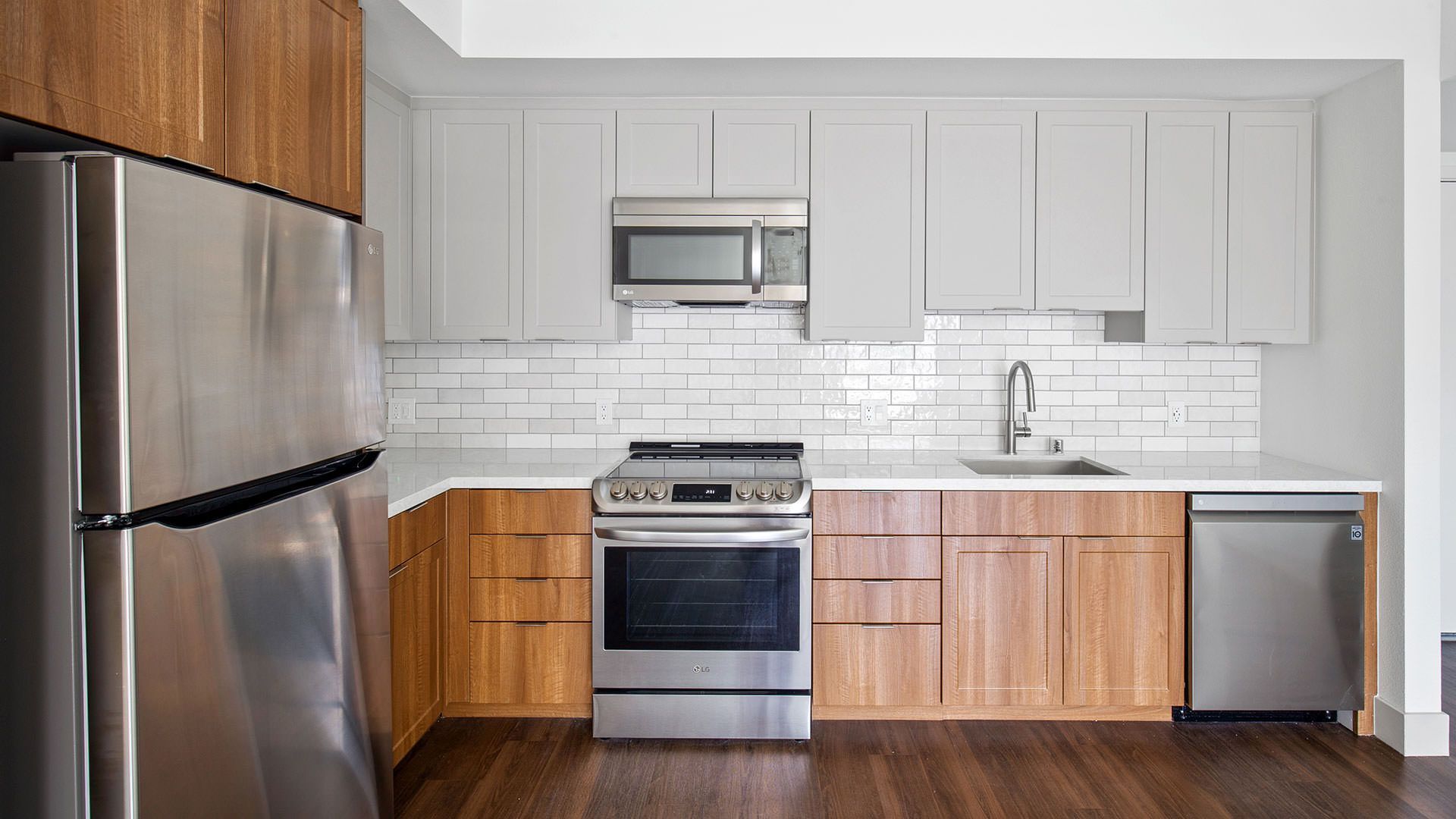 Modern kitchen with stainless steel appliances, wooden and gray cabinets, and white tile backsplash at The Waymark in Walnut Creek, CA.