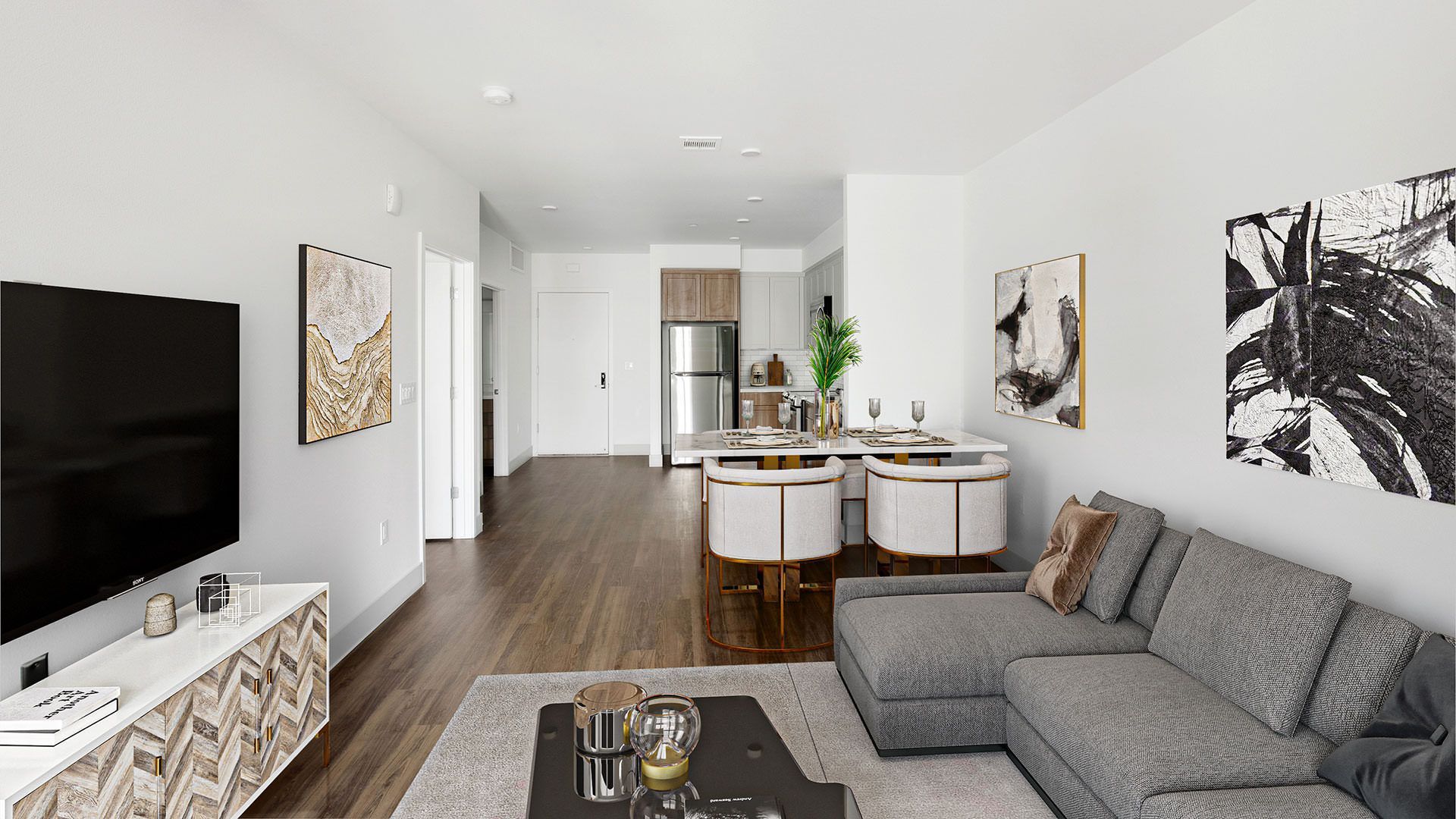 Modern apartment living room with grey sectional, TV, and open kitchen area at The Waymark in Walnut Creek, CA.