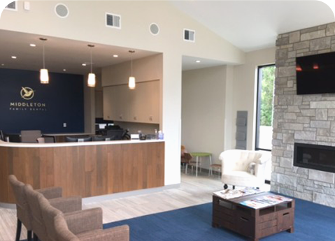 Modern dental office lobby with a wood reception desk, navy blue accent wall, stone fireplace, and waiting area chairs.
