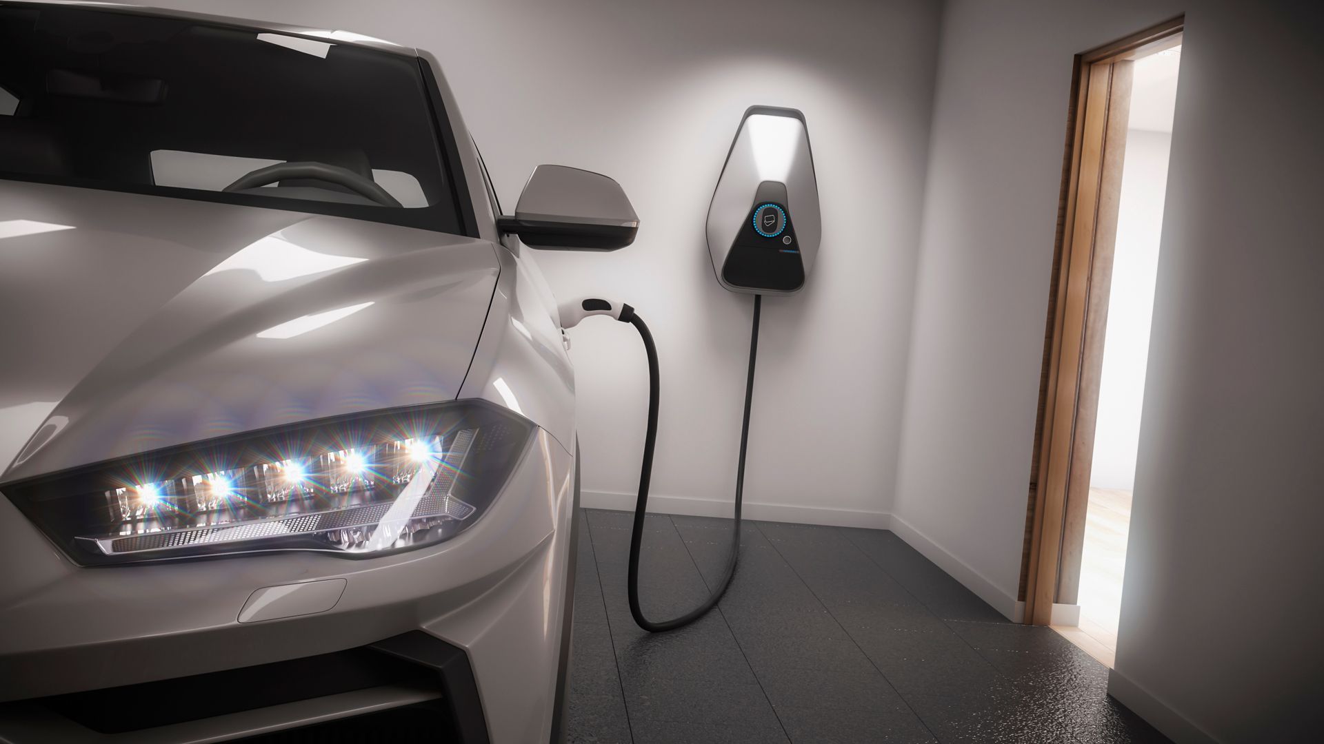 A silver electric vehicle parked in a garage, plugged into a wall-mounted charging station.