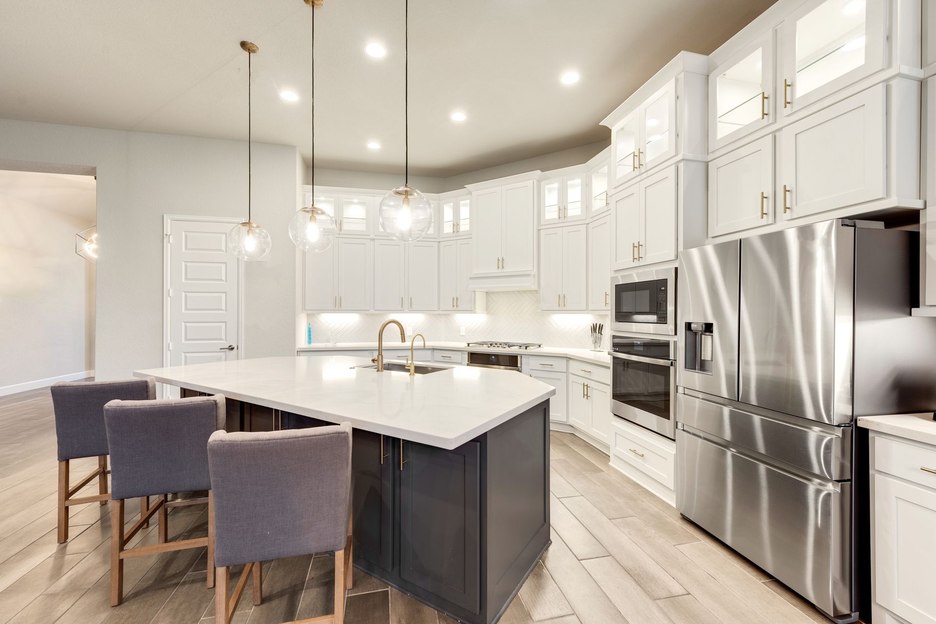 A bright modern kitchen with a dark gray island, white cabinetry, stainless steel appliances, and three bar stools.