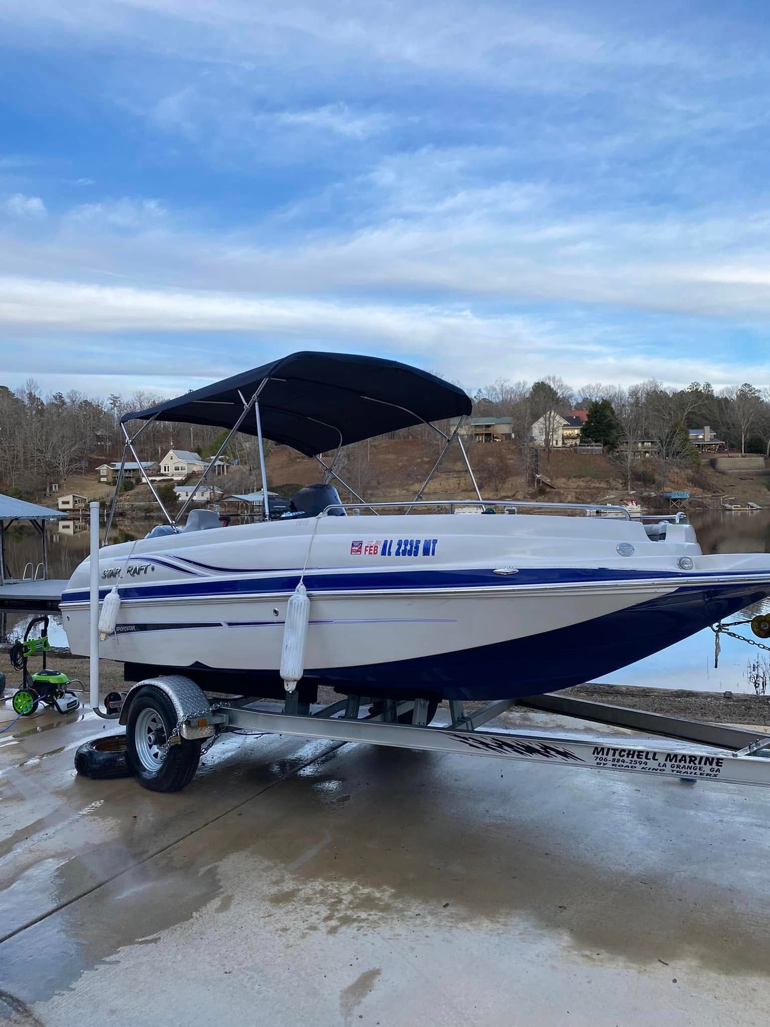 White and blue speedboat on a trailer in a snowy driveway under a cloudy sky