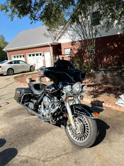 Black motorcycle parked in a driveway in front of a brick house on a sunny day