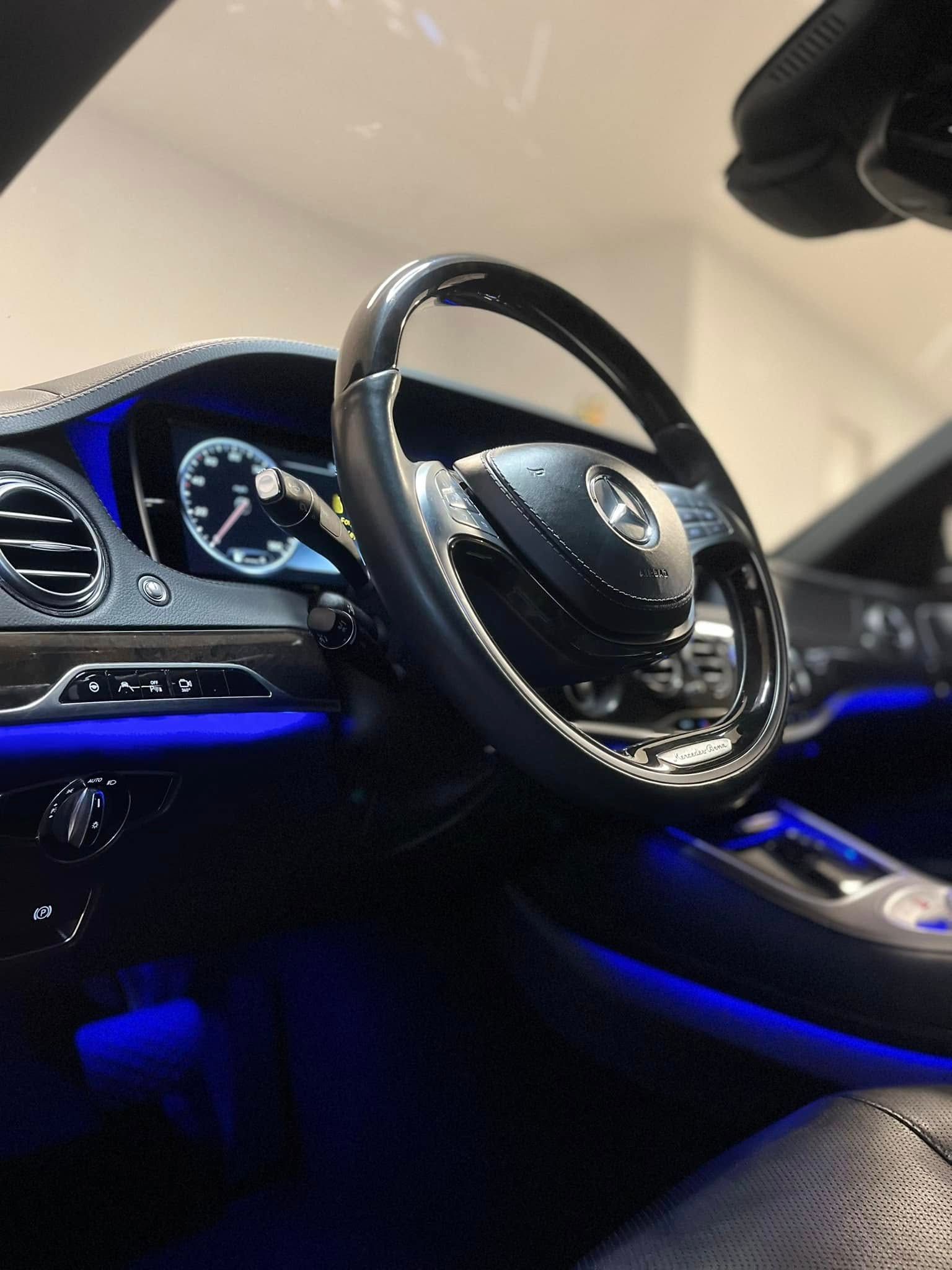 Luxury car interior with black leather seats, blue ambient lighting, and a chrome steering wheel dashboard view
