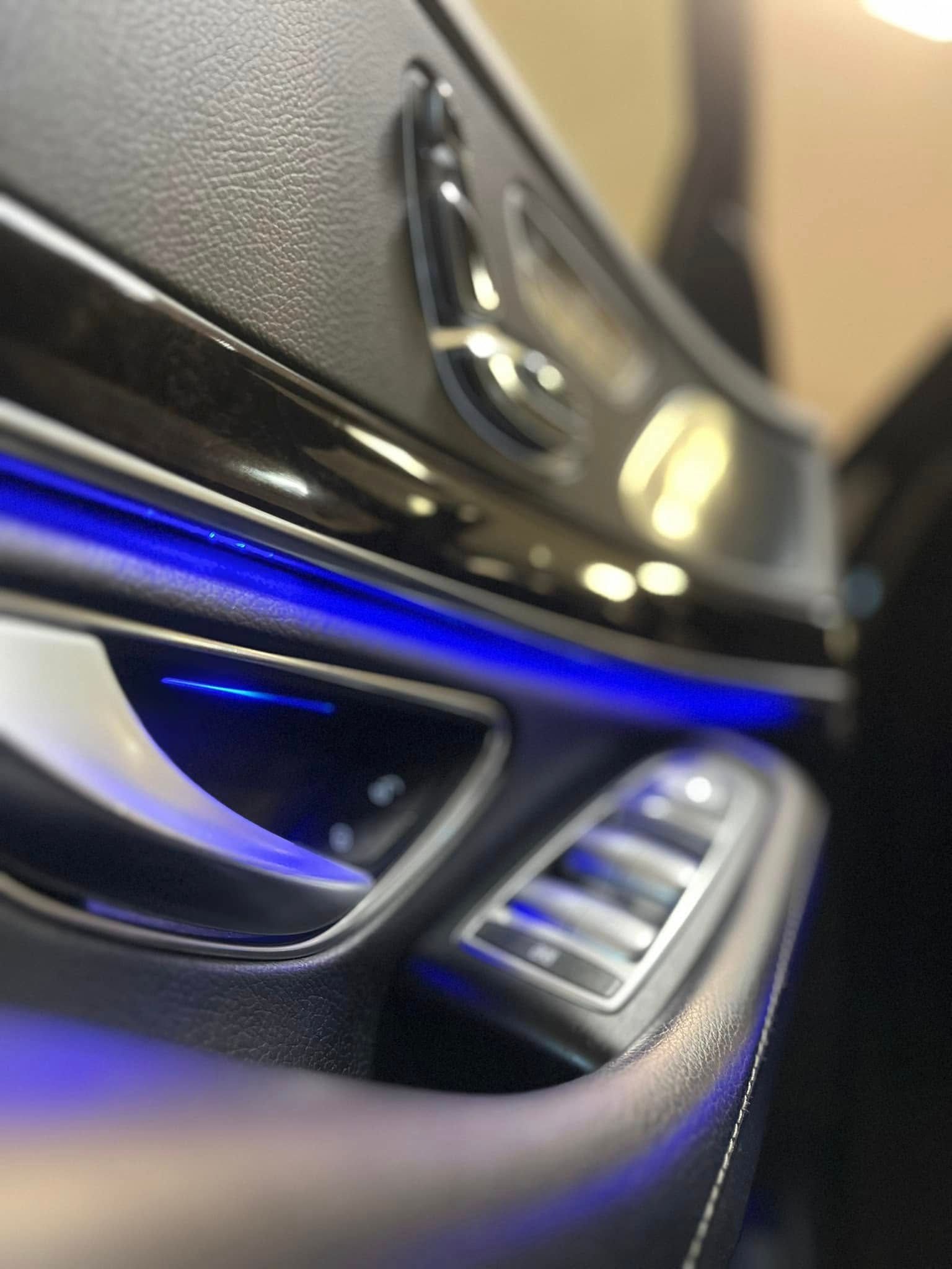 Close-up of a car interior door panel with blue ambient lighting and silver air vent trim