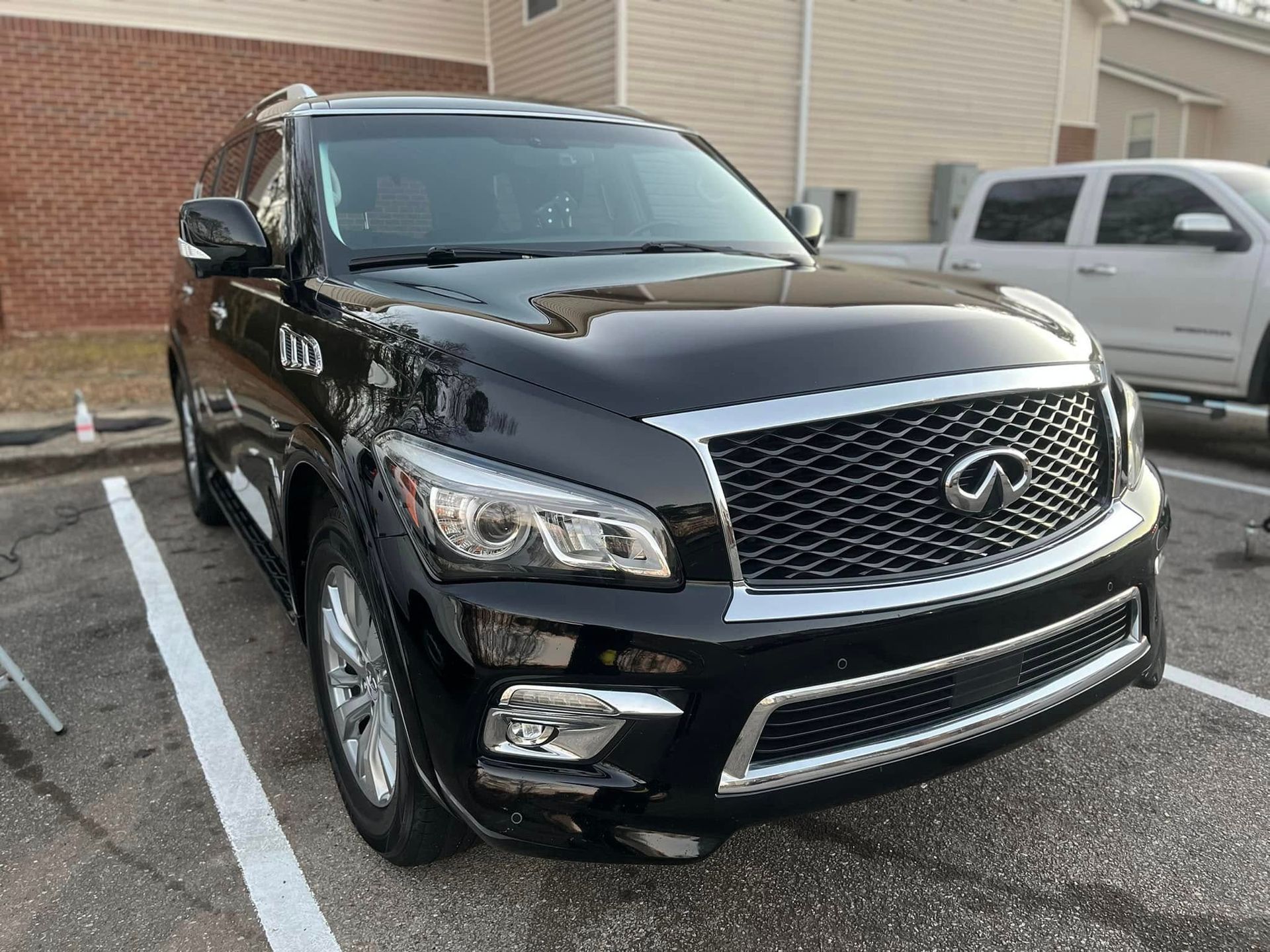 Black Infiniti SUV parked beside a brick building in a lot
