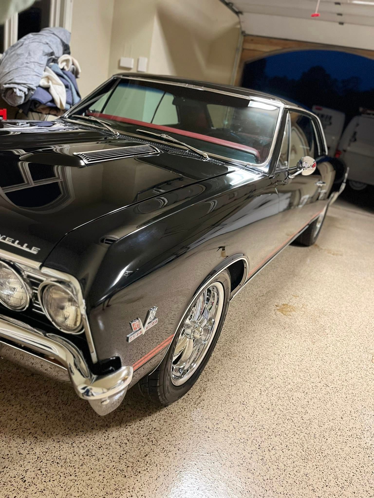 Black classic car parked in a garage, front-left view, with chrome trim and red windshield stripe