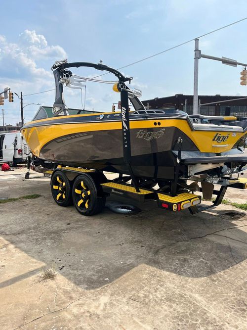 Yellow-and-black boat on a trailer in a parking lot under a bright sky