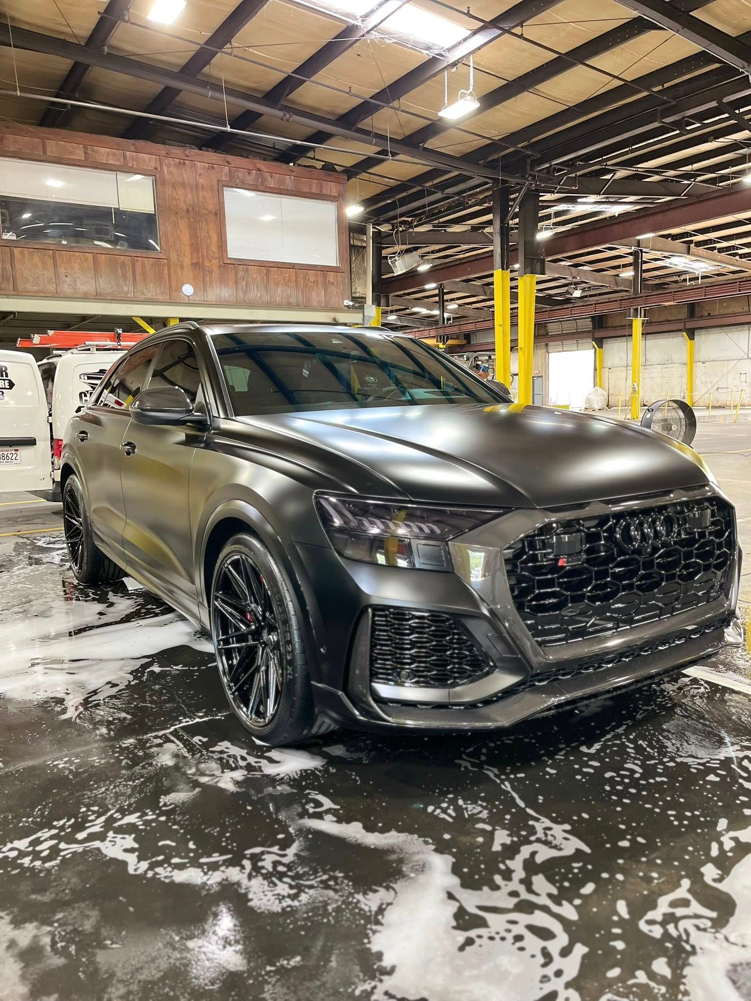 Dark gray sports SUV in a wet warehouse with snow on the floor and white vehicles behind it