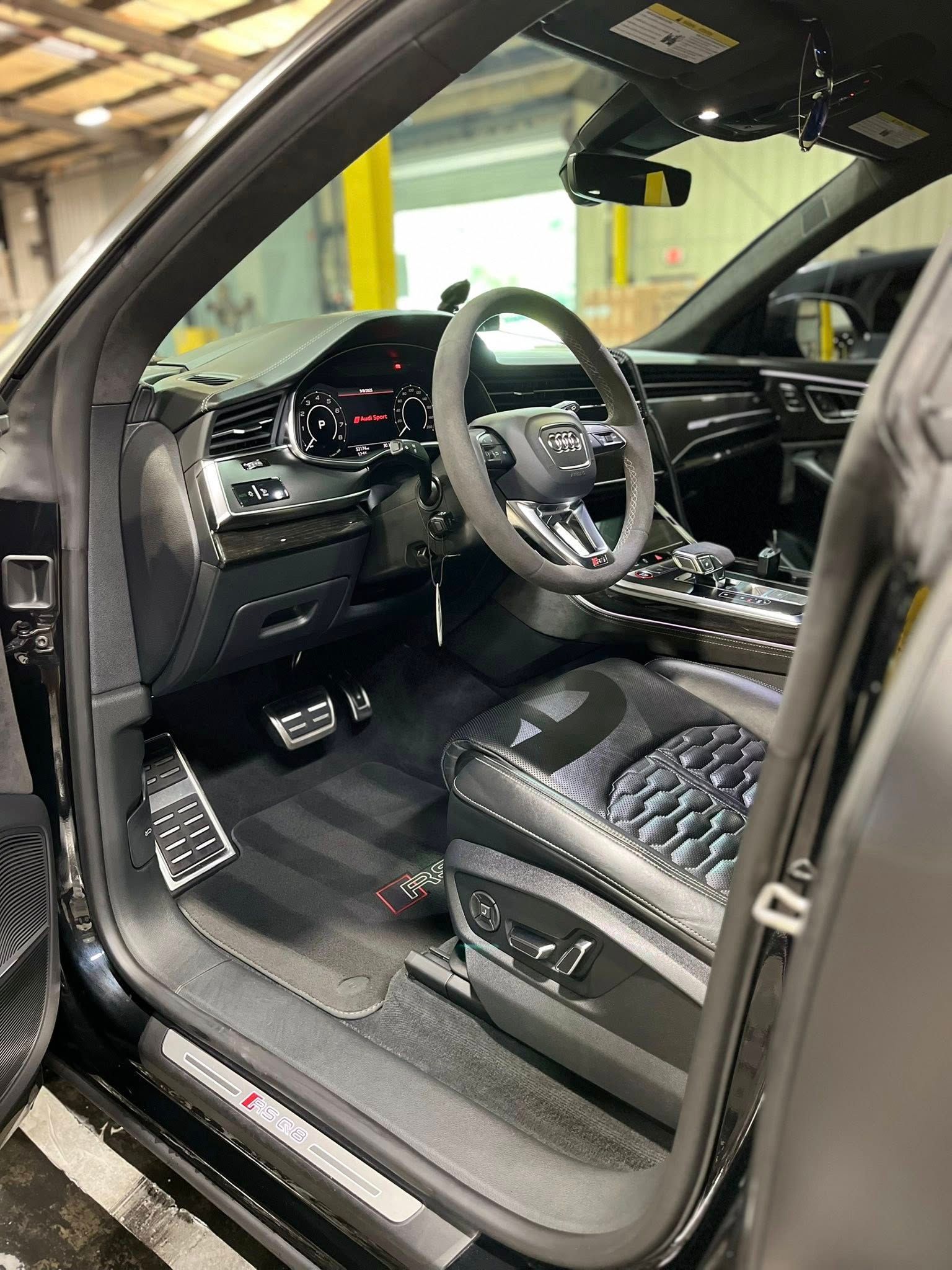 Luxury car interior with open door, black leather seats, and illuminated dashboard