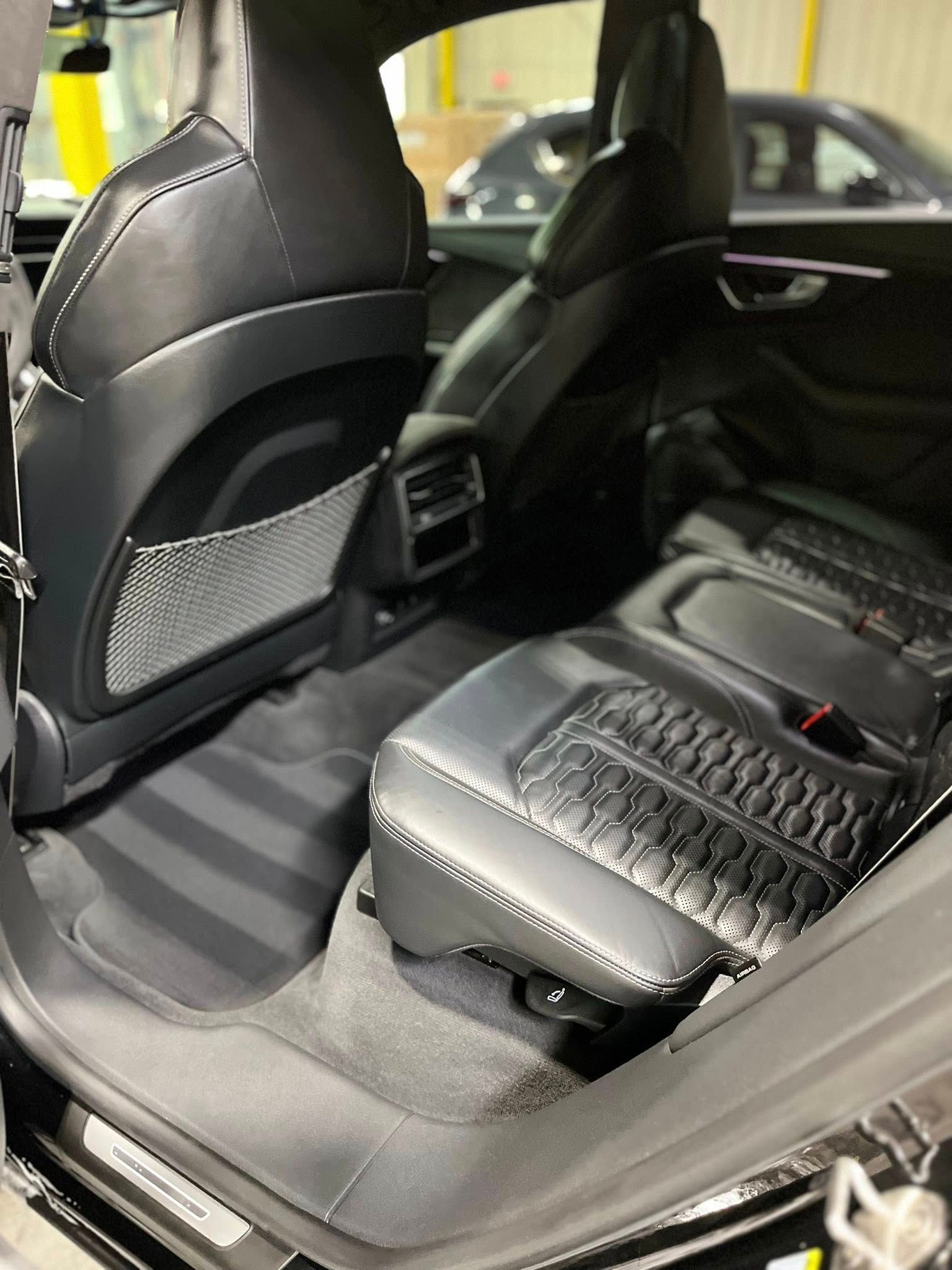 Car interior with black leather rear seats and quilted seat covers, viewed from the open door