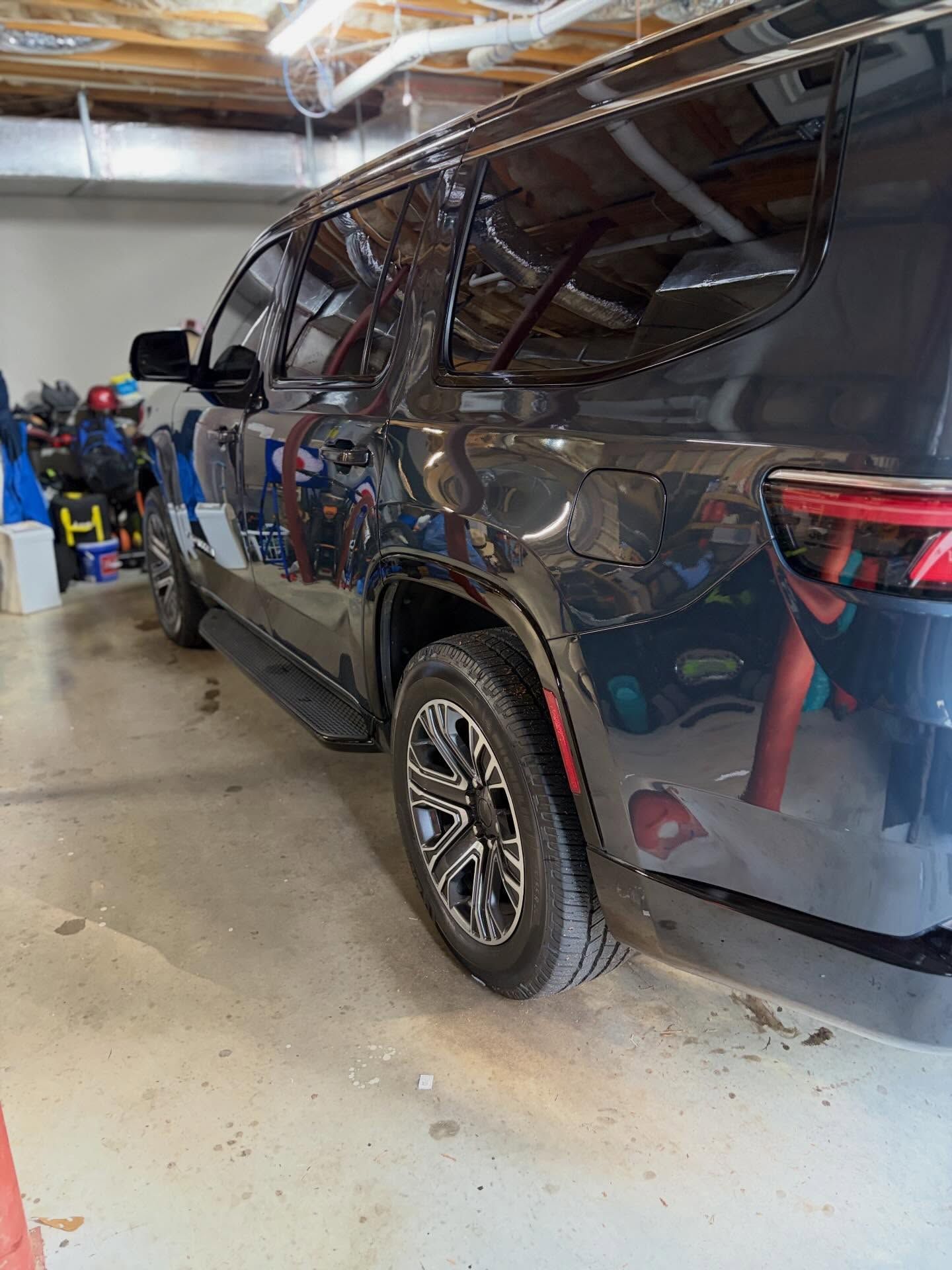 Dark blue SUV parked in a garage, rear side view with storage items along the wall