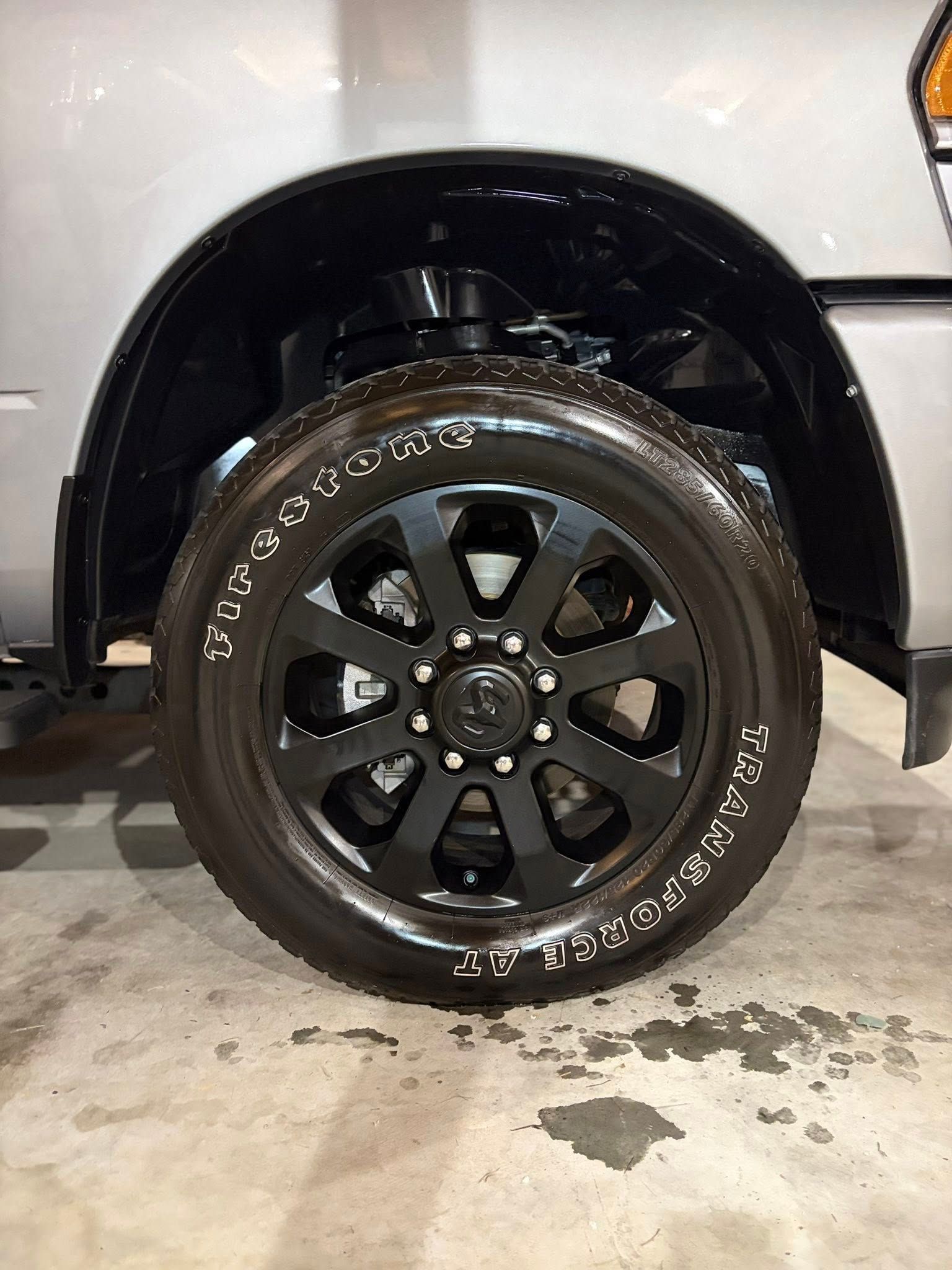 Black off-road wheel and tire on a white truck with a wet concrete ground underneath
