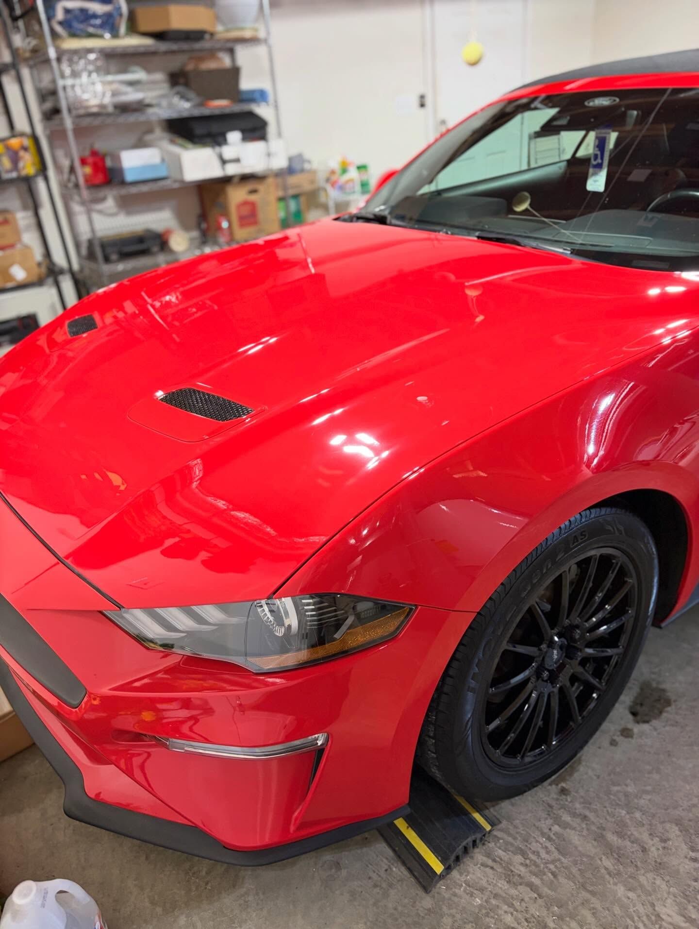 Red sports car in a garage, front-left view, with black wheels and a glossy finish