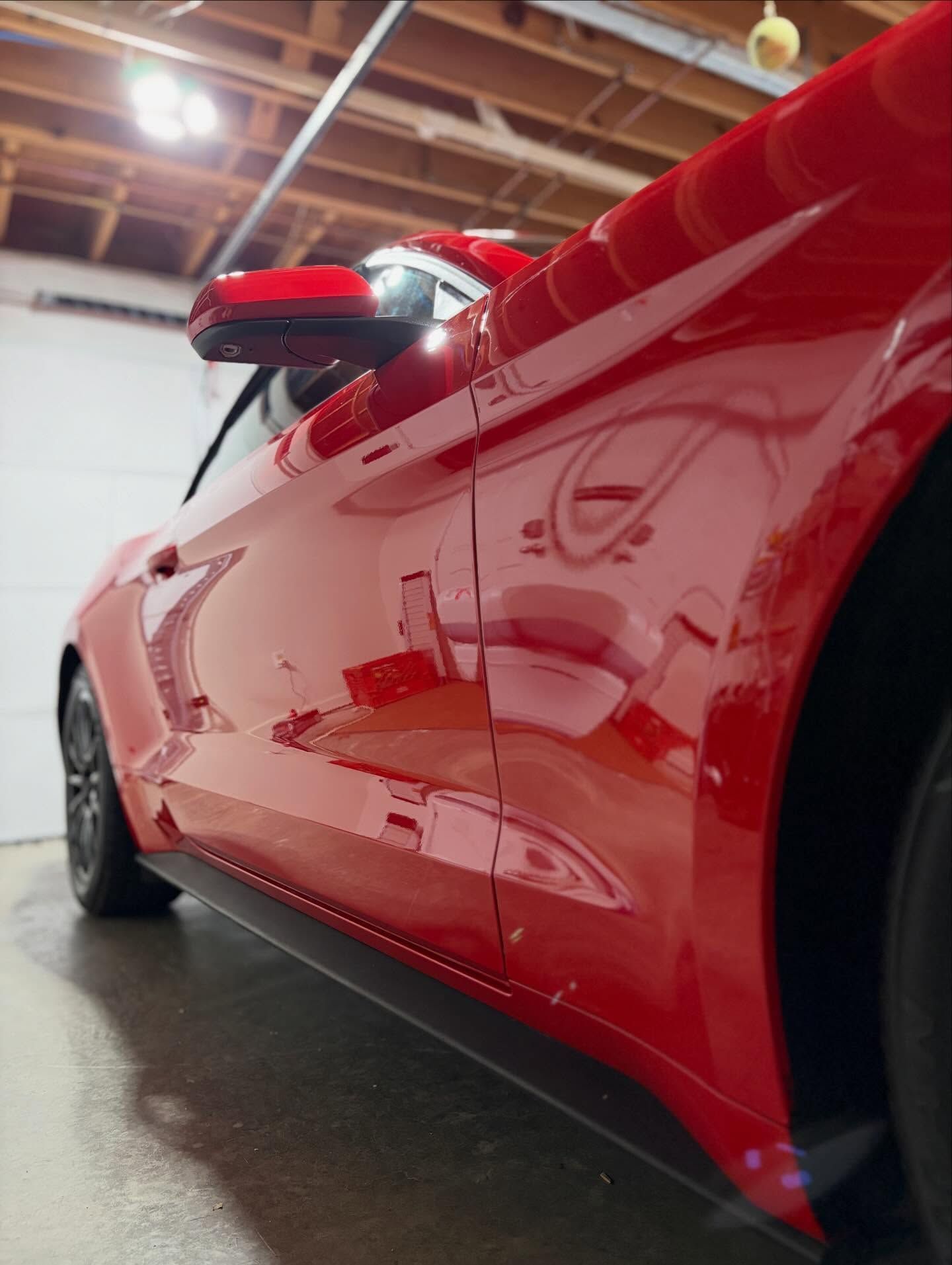 Red sports car viewed from the side in a garage, with glossy reflections on the body.