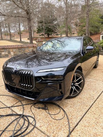 Black BMW sedan parked on a driveway, front three-quarter view, with trees in the background.