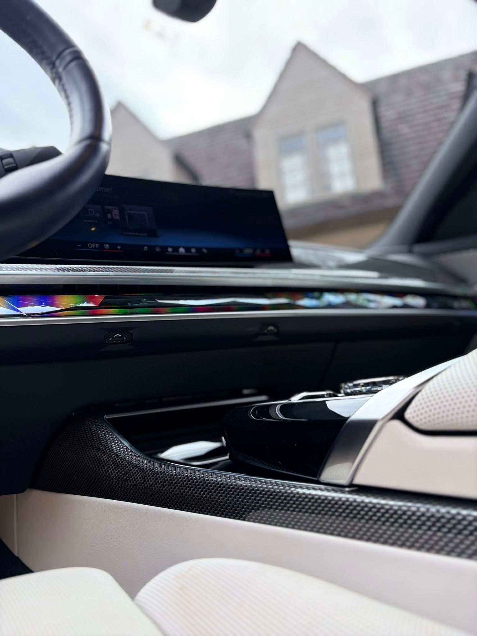 Luxury car interior with dashboard screen, glossy trim, and beige seats, parked near houses outdoors
