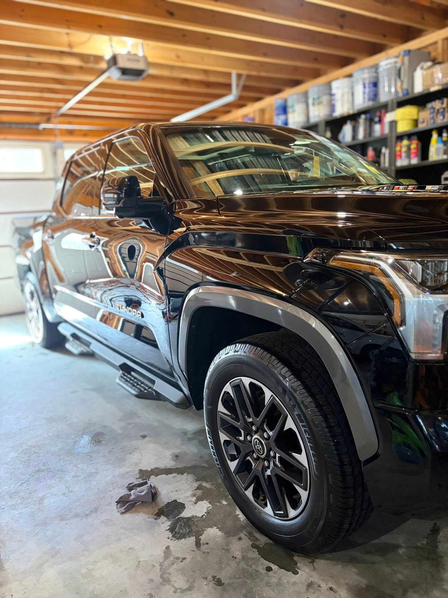 Black SUV parked in a garage, with wet floor and shelves of supplies in the background