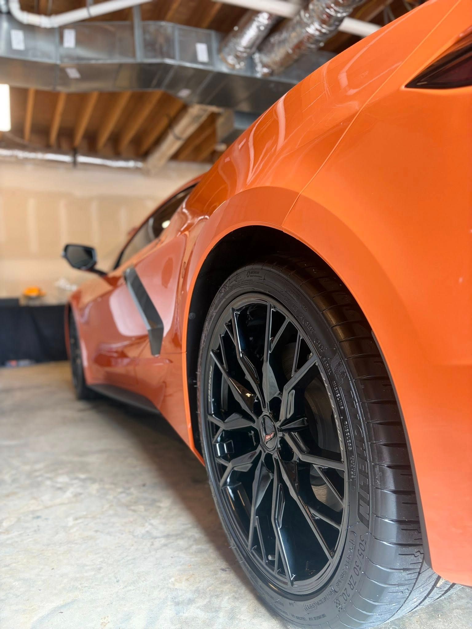 Orange sports car with black wheels parked in a garage, low-angle close-up view