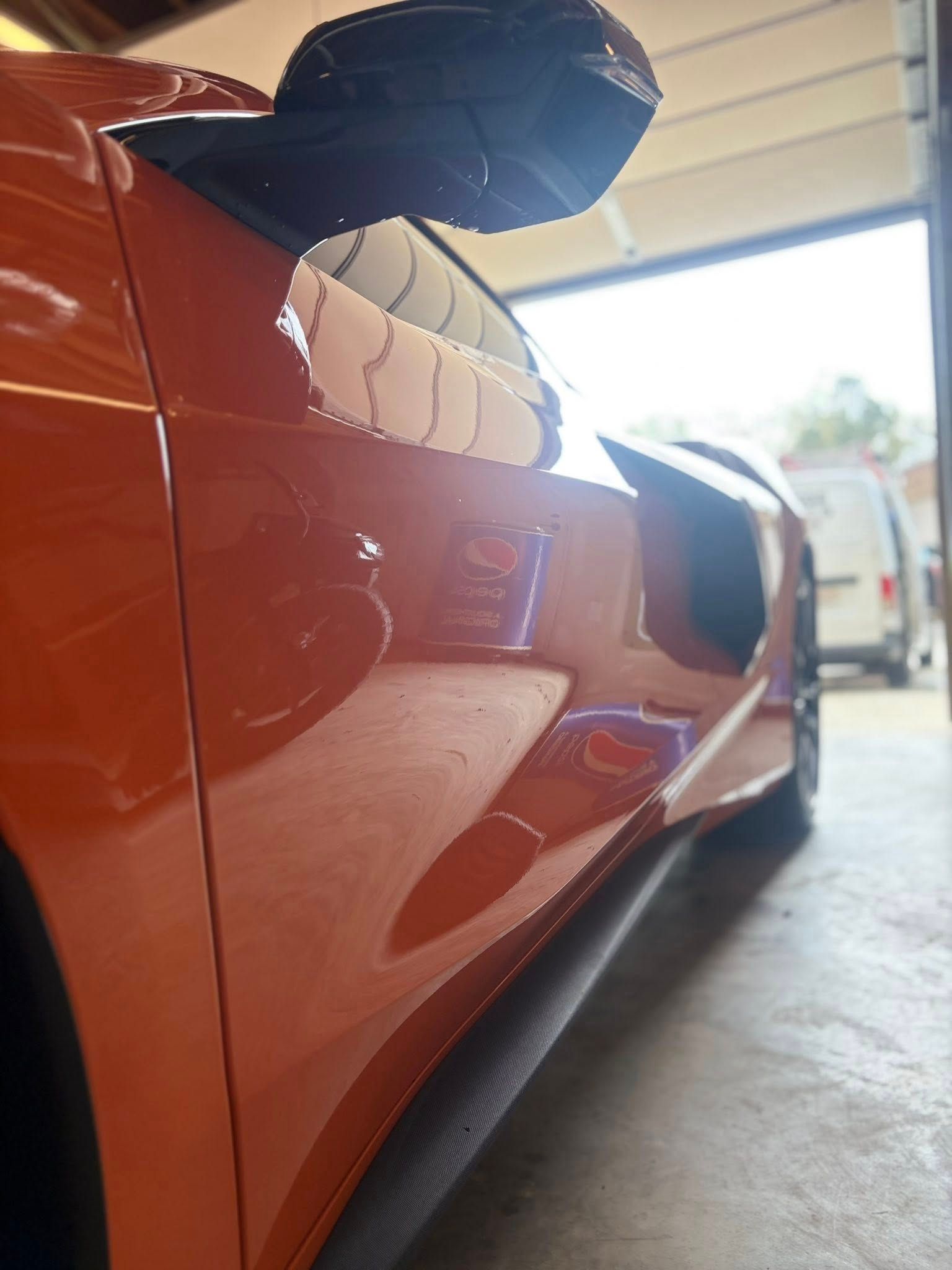 Close-up of an orange sports car in a garage, showing the side mirror and sleek body lines.