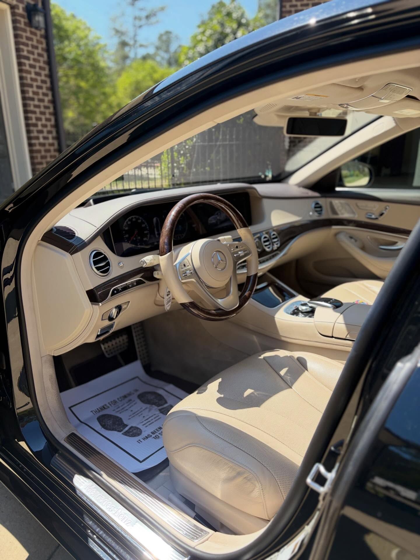 Luxury car interior with beige seats and open driver door, showing steering wheel and dashboard.