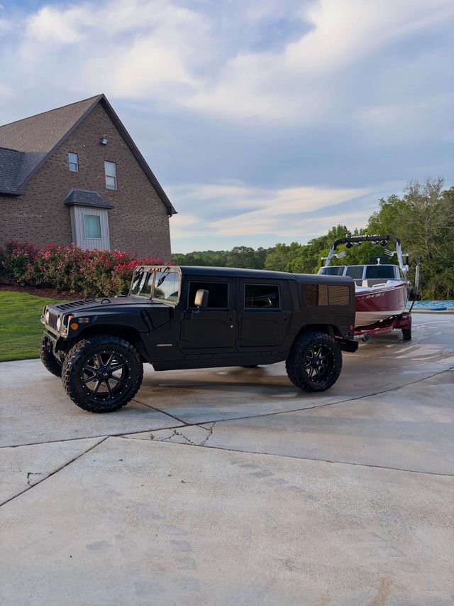 Black lifted SUV parked in a driveway beside a brick house, with a red boat/trailer behind it.