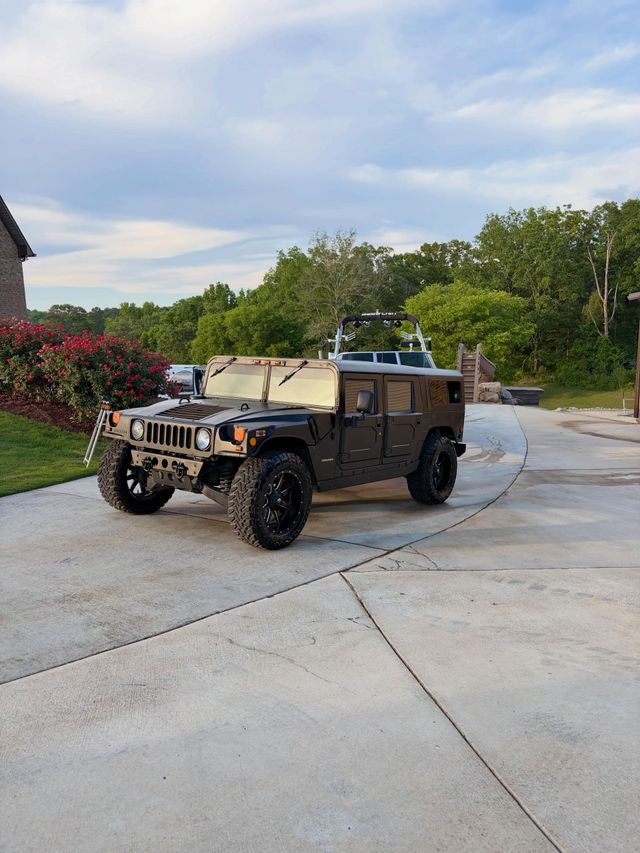 Camouflaged Humvee parked on a curved driveway beside trees and shrubs.