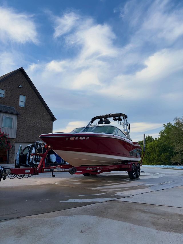 Red and white speedboat on a trailer in a parking lot beside a brick building under a cloudy sky